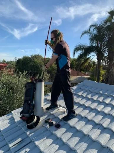 Roof technician feeding flue-cleaning equipment into a chimney